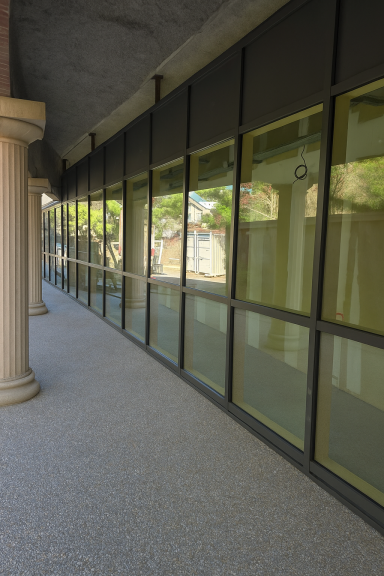 Couloir avec des colonnes et des fenêtres vitrées, éclairé par la lumière naturelle.